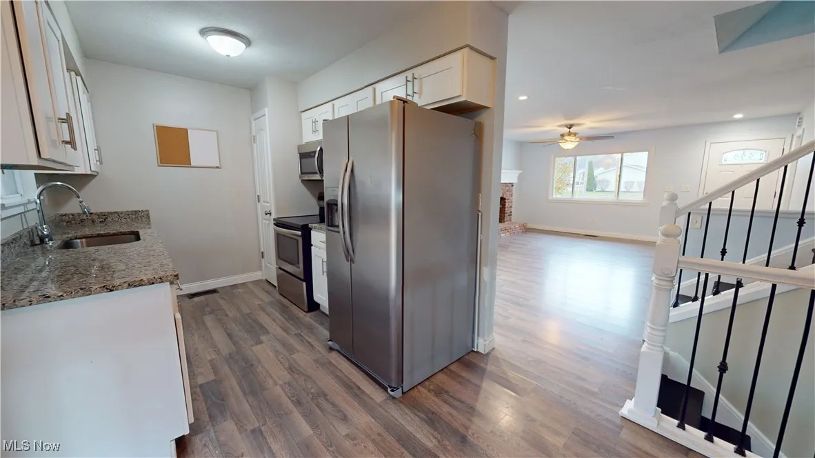 Kitchen featuring light stone countertops, appliances with stainless steel finishes, white cabinetry, a ceiling fan, and dark wood finished floors