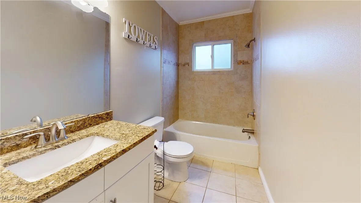 Bathroom featuring vanity, bathtub / shower combination, light tile patterned floors, and ornamental molding