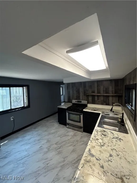 Kitchen featuring stove, dark cabinets, light countertops, light marble finish flooring, and wood walls
