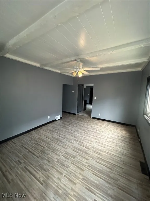Unfurnished room with wood finished floors, beam ceiling, and ceiling fan