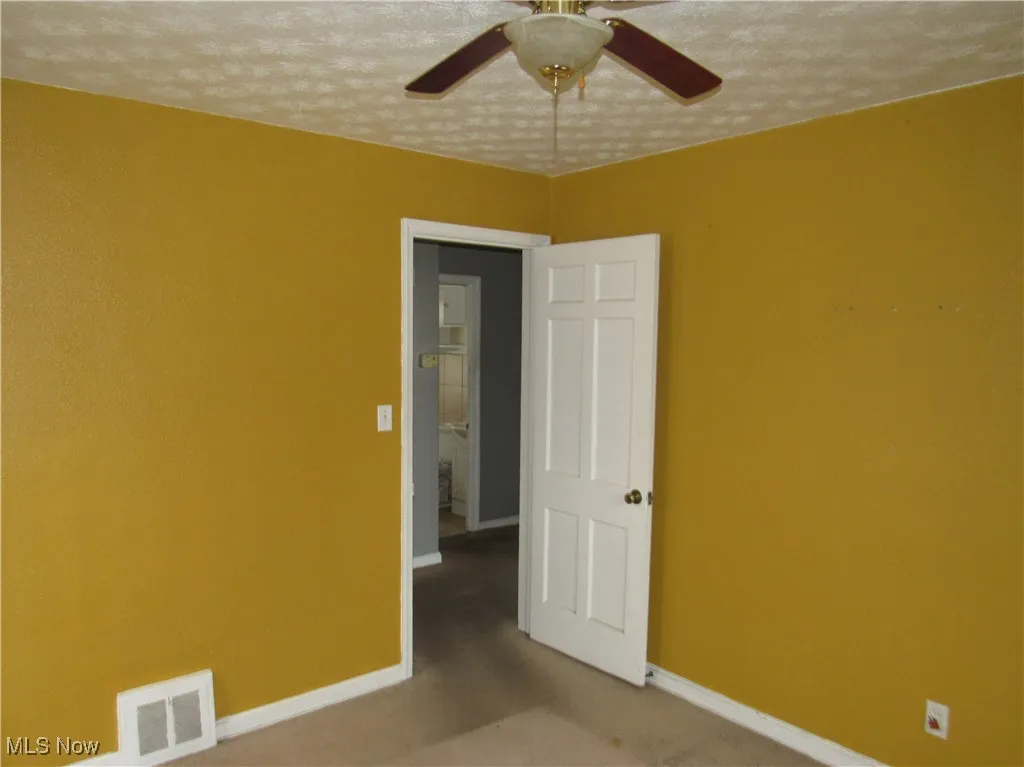 Carpeted spare room featuring a textured ceiling and ceiling fan