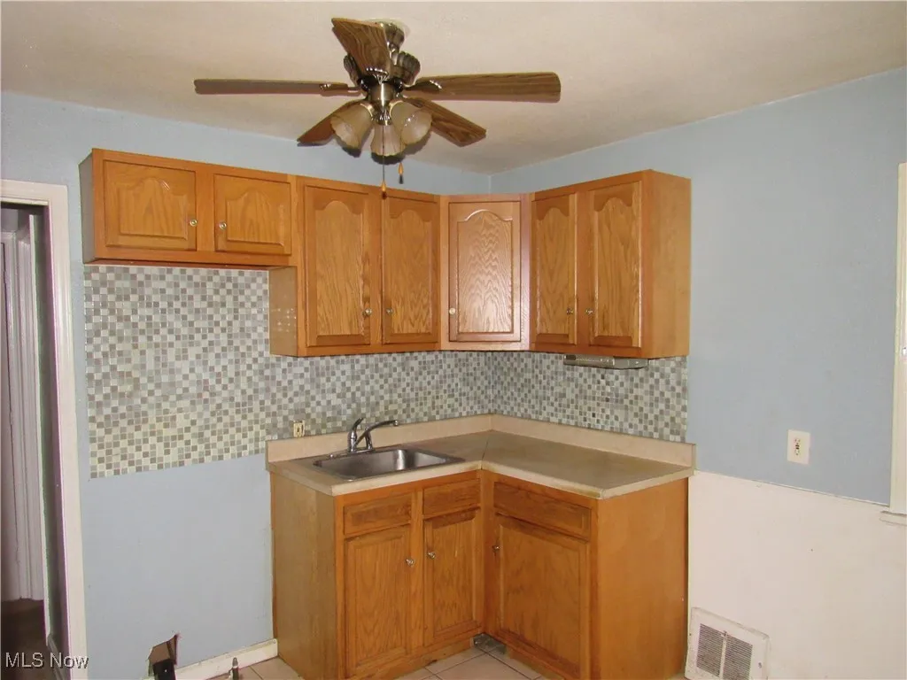 Kitchen with decorative backsplash, light countertops, brown cabinets, a ceiling fan, and light tile patterned flooring