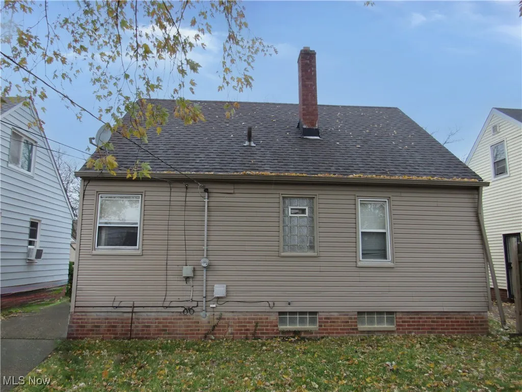 Back of property featuring a chimney, a shingled roof, and a lawn