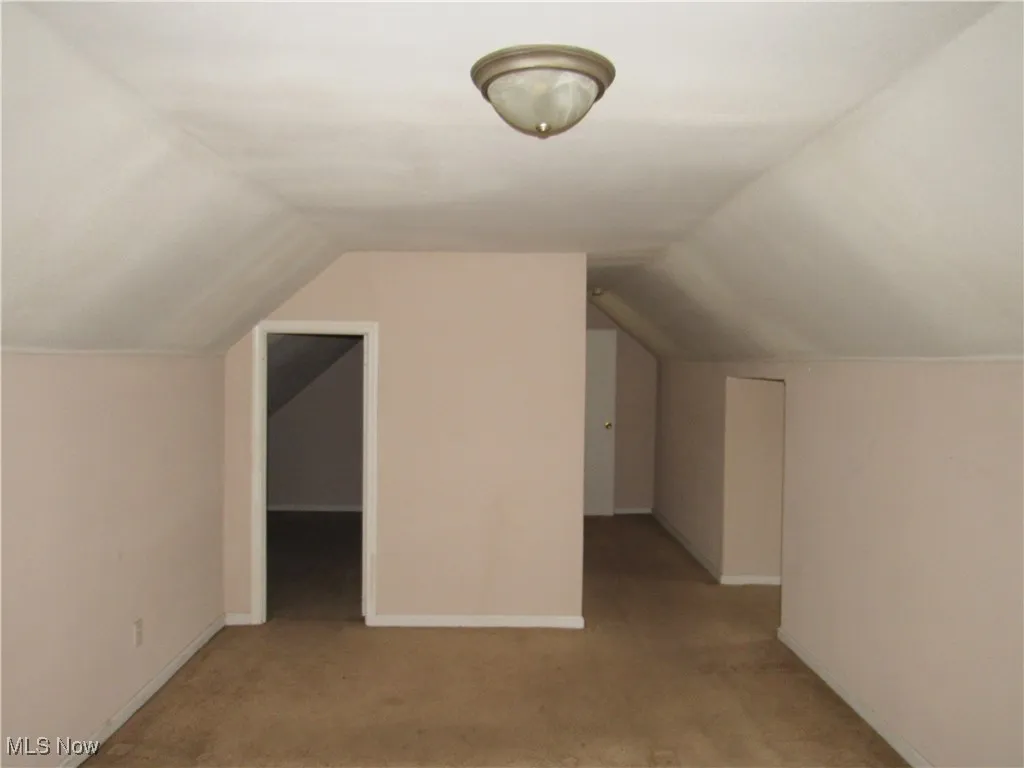 Additional living space with vaulted ceiling and light carpet