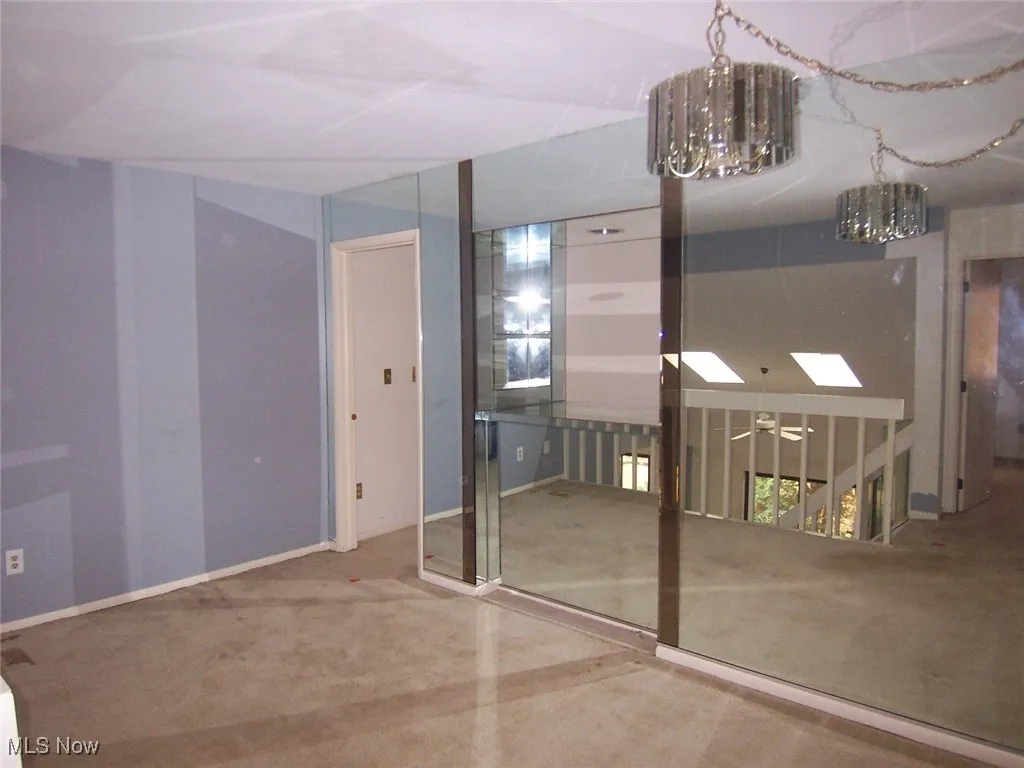 Carpeted loft with a chandelier and mirror wall