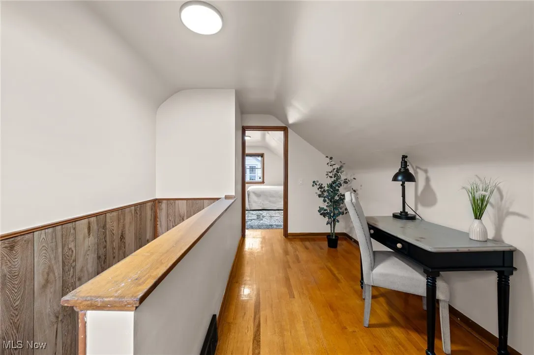 Hall with an upstairs landing, light wood-style floors, and lofted ceiling
