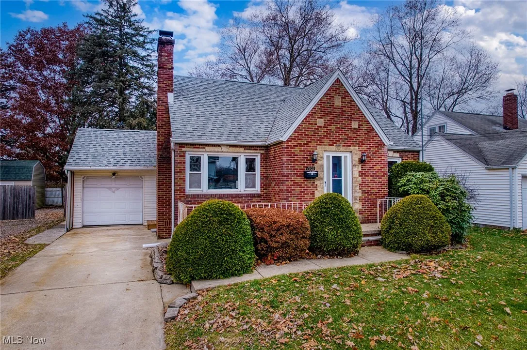 View of front of home with roof with shingles, driveway, brick siding, a chimney, and a garage