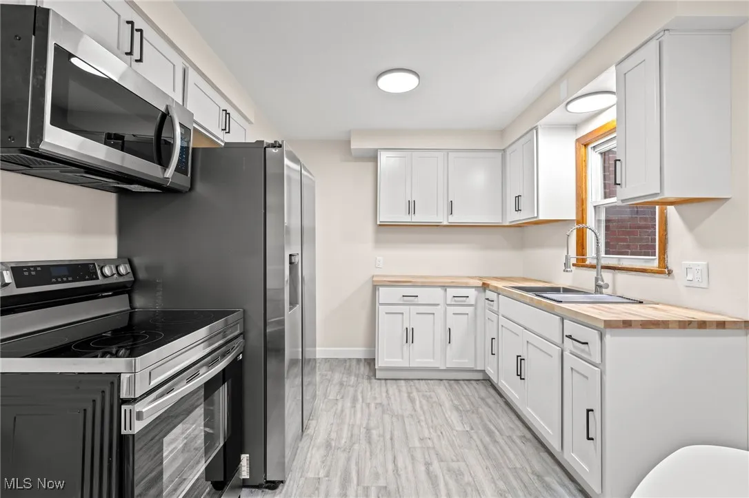 Kitchen with stainless steel appliances, butcher block countertops, and white cabinetry