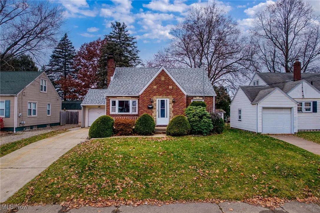 Bungalow-style home featuring brick siding, a chimney, a front yard, a garage, and driveway