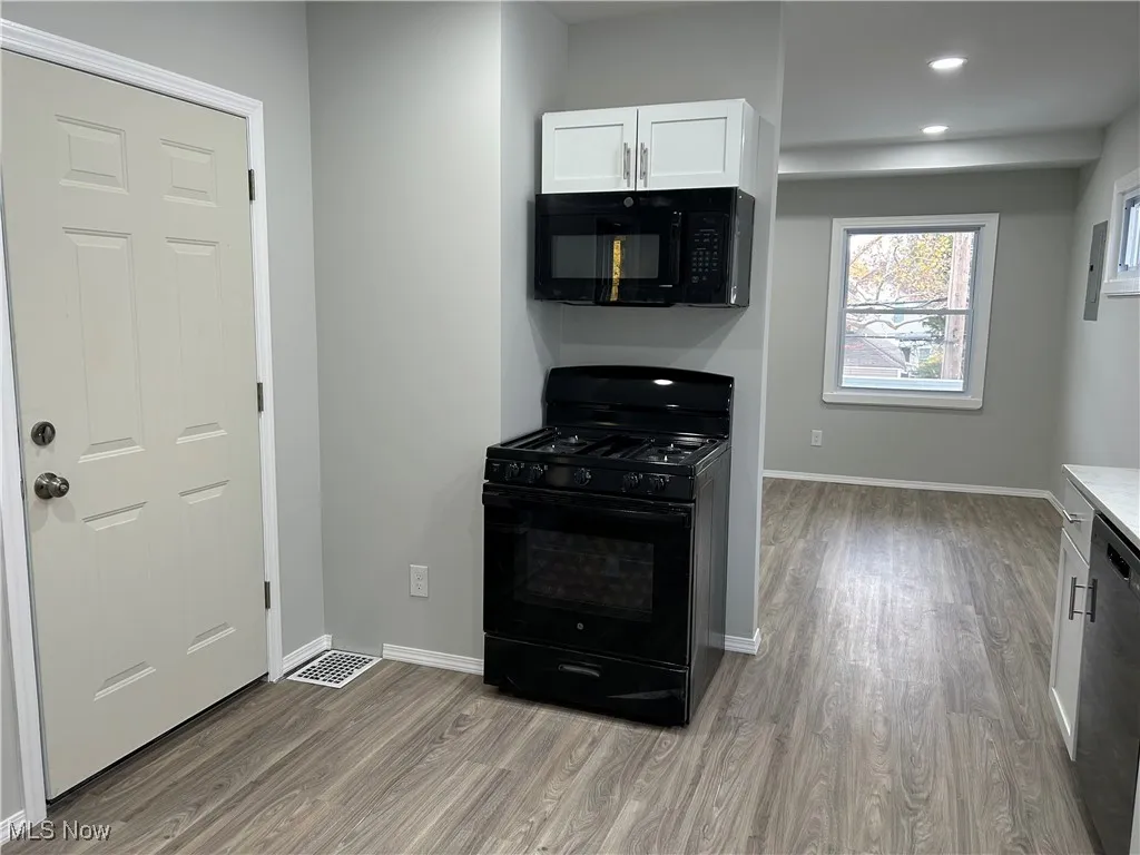 Kitchen with black appliances, white cabinetry, light wood-type flooring, and recessed lighting