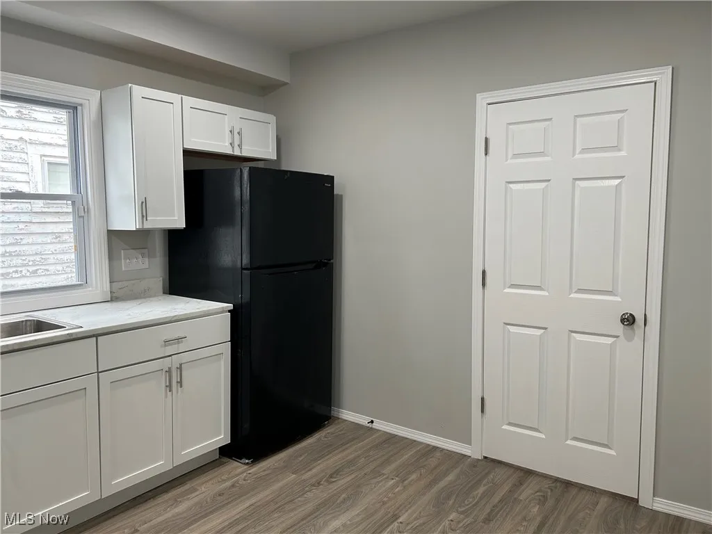 Kitchen with white cabinetry, light wood-style floors, freestanding refrigerator, and light stone countertops