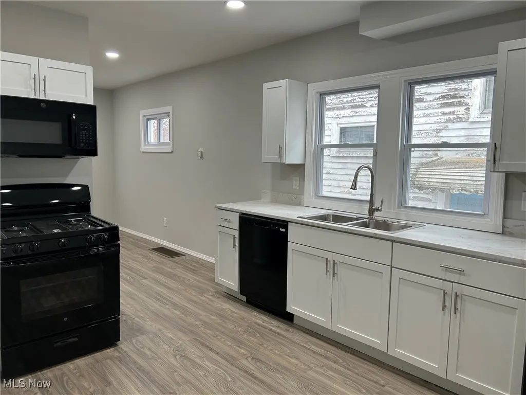 Kitchen with black appliances, white cabinetry, light wood-style flooring, and recessed lighting