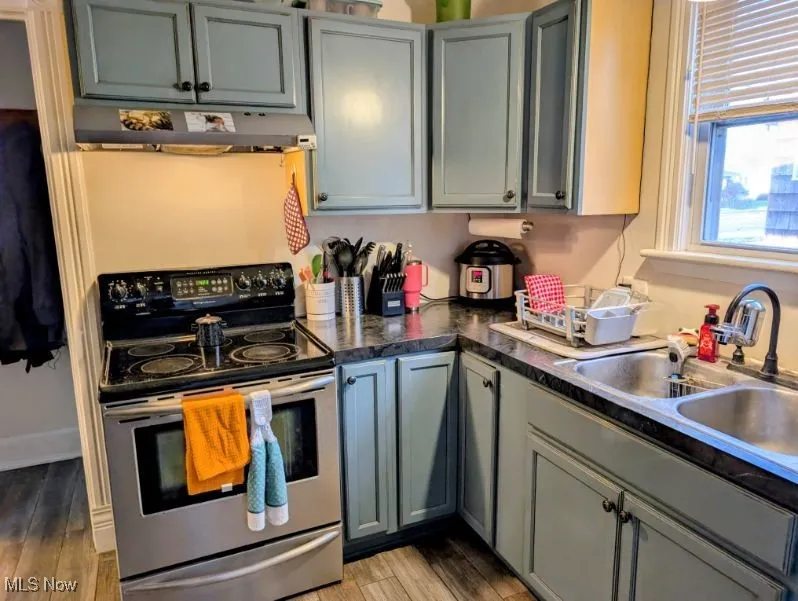 Kitchen featuring stainless steel range with electric stovetop, dark countertops, under cabinet range hood, light wood-style floors, and gray cabinets