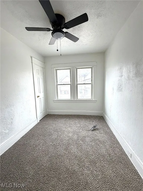 Carpeted spare room featuring a textured wall, a textured ceiling, and a ceiling fan
