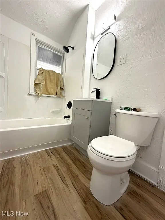 Bathroom with a textured wall, vanity, a textured ceiling, washtub / shower combination, and light wood-style flooring