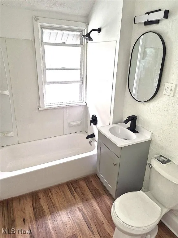 Full bath with dark wood-style floors, washtub / shower combination, vanity, and a textured wall