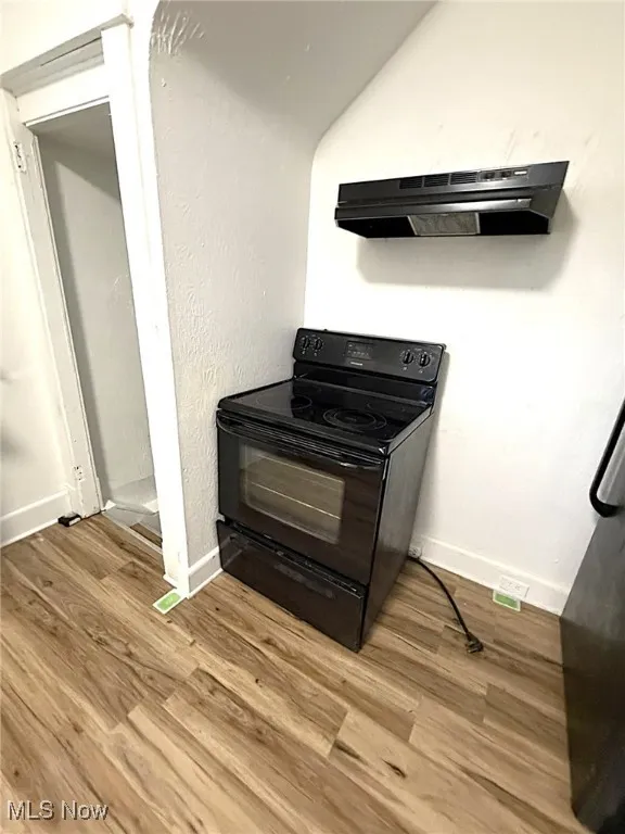 Kitchen with black range with electric cooktop, under cabinet range hood, light wood finished floors, and a textured wall