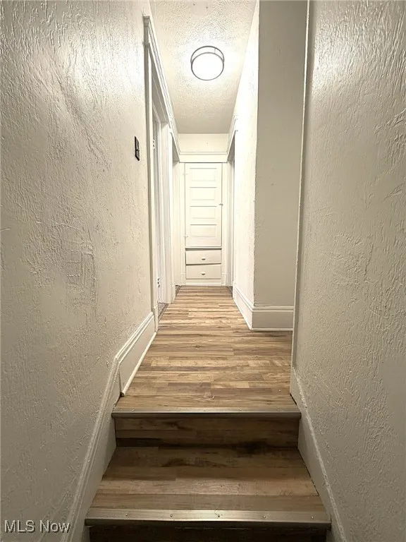 Stairs with a textured wall, wood finished floors, and a textured ceiling