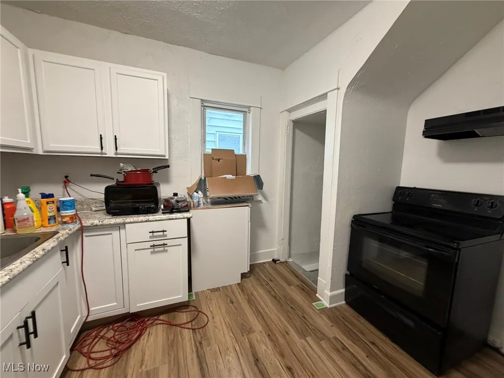 Kitchen featuring white cabinetry, black range with electric stovetop, a textured ceiling, dark wood finished floors, and extractor fan