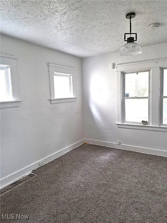Spare room featuring a textured ceiling, dark colored carpet, and a smoke detector