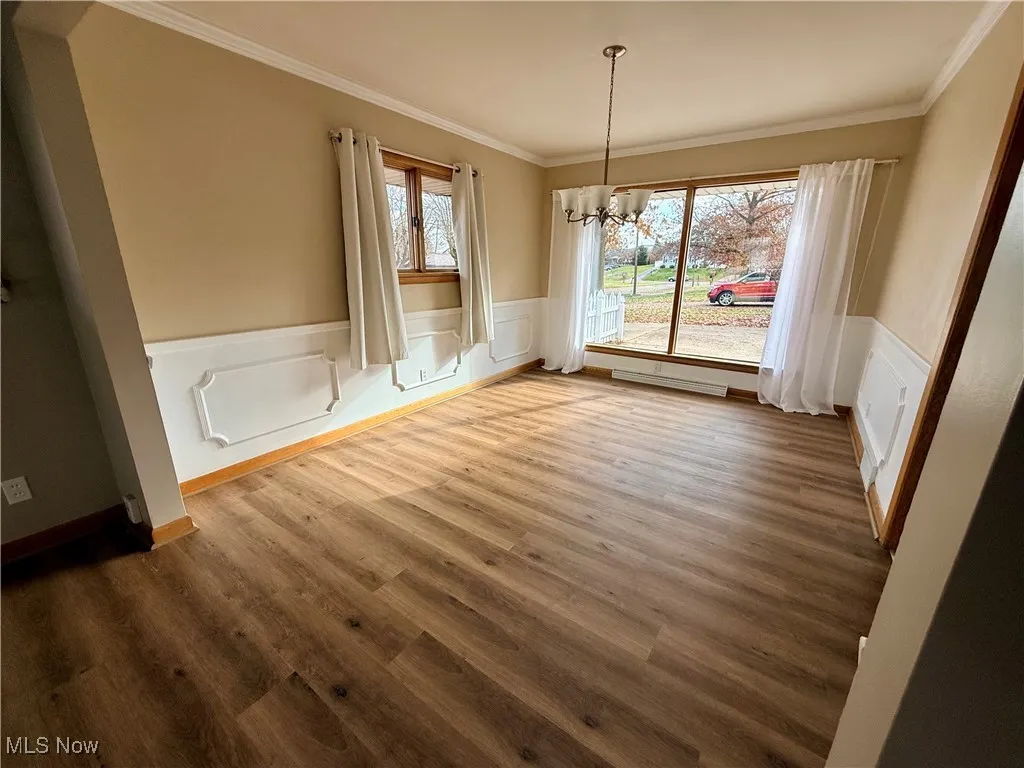  Dining area with wainscoting, a chandelier, large picture window, crown molding, and newly installed LVP floors.