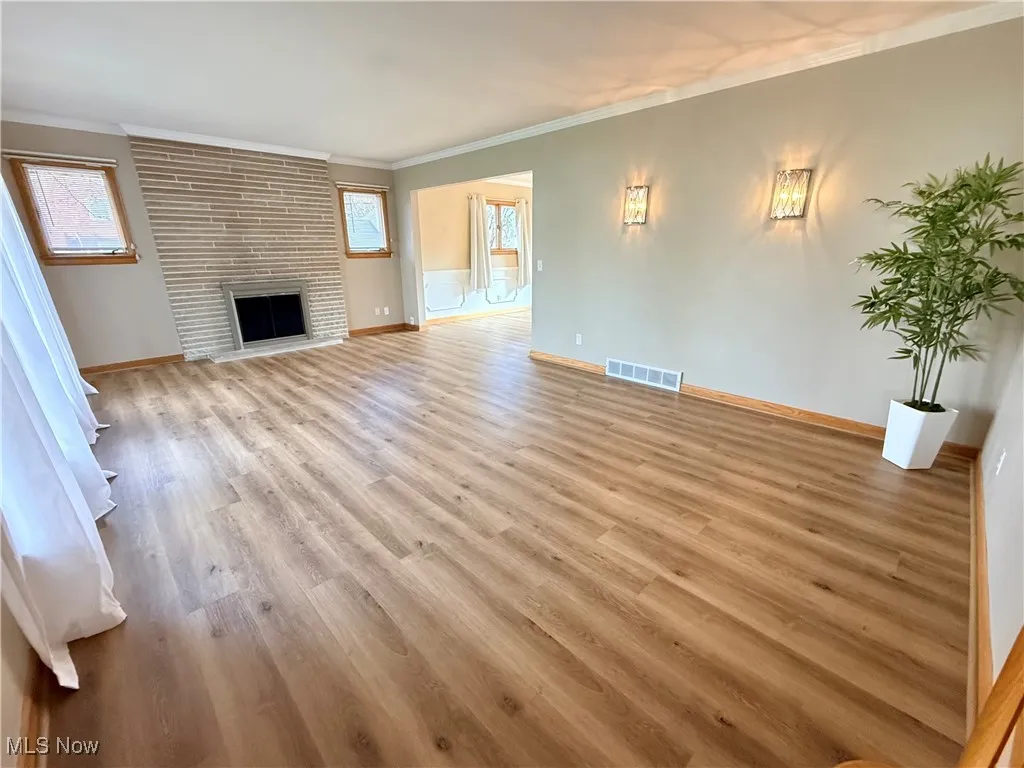  Living room featuring newly installed LVP flooring, a stone fireplace, and crown molding