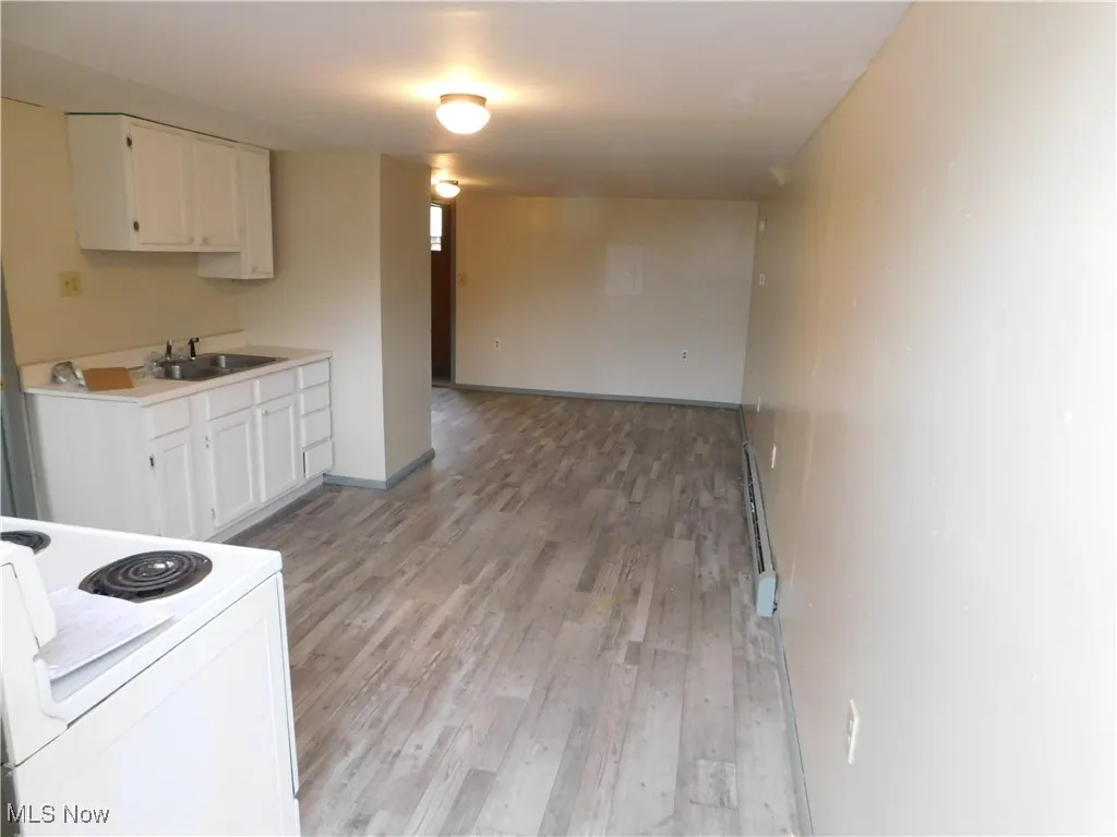 Kitchen featuring electric range, light countertops, white cabinets, and light wood-style flooring