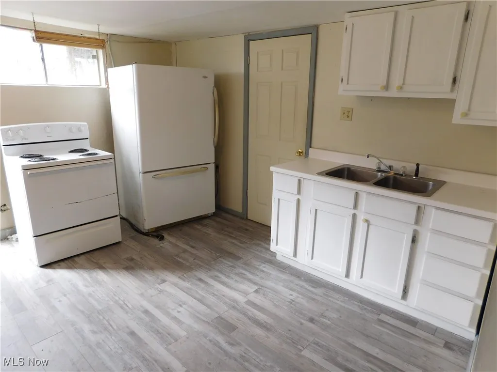 Kitchen with white appliances, light countertops, white cabinets, and light wood-style flooring