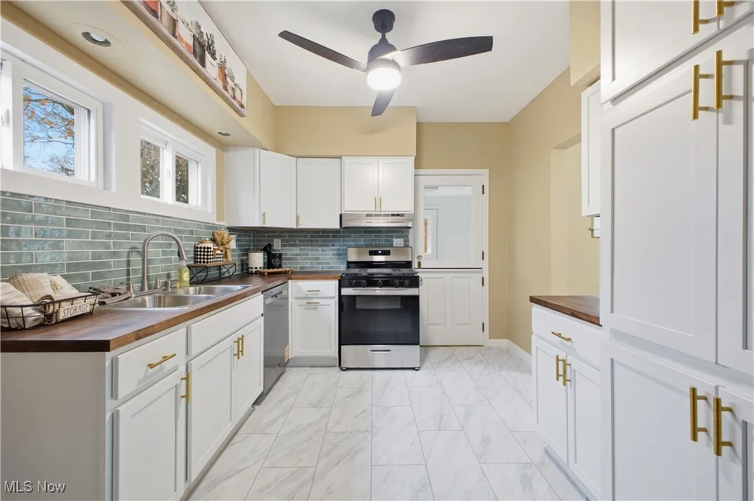 Kitchen with wooden counters, appliances with stainless steel finishes, white cabinetry, light marble finish flooring, and a ceiling fan