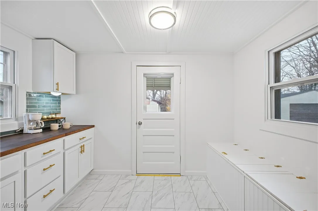 Kitchen with butcher block counters, white cabinets, and light marble finish floors