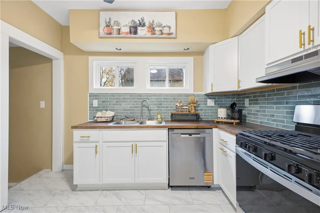 Kitchen with black range with gas cooktop, stainless steel dishwasher, wooden counters, and white cabinets