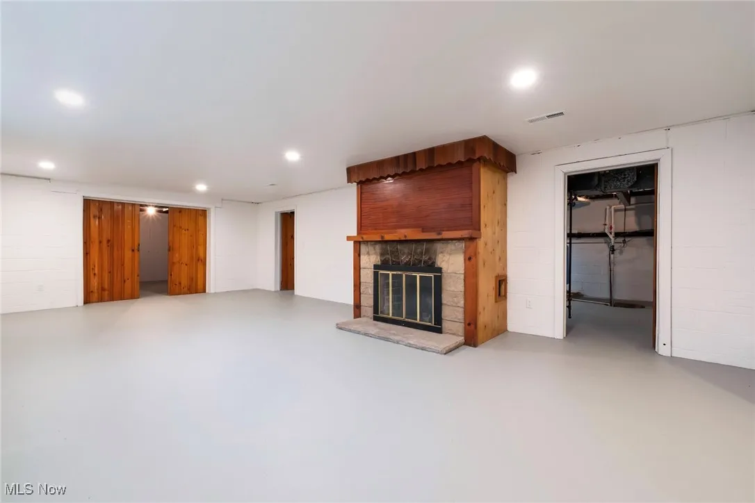 Unfurnished living room with concrete block wall, finished concrete flooring, and a stone fireplace