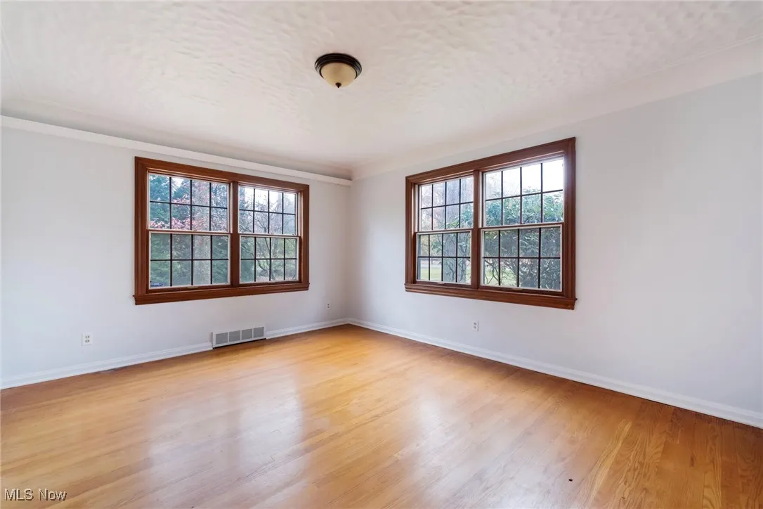 Spare room featuring light wood-type flooring, healthy amount of natural light, a textured ceiling, and ornamental molding