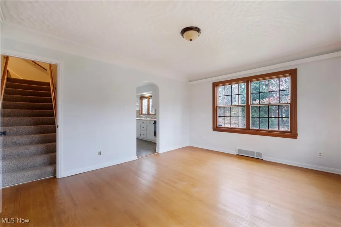 Empty room with arched walkways, ornamental molding, light wood-style floors, and stairs