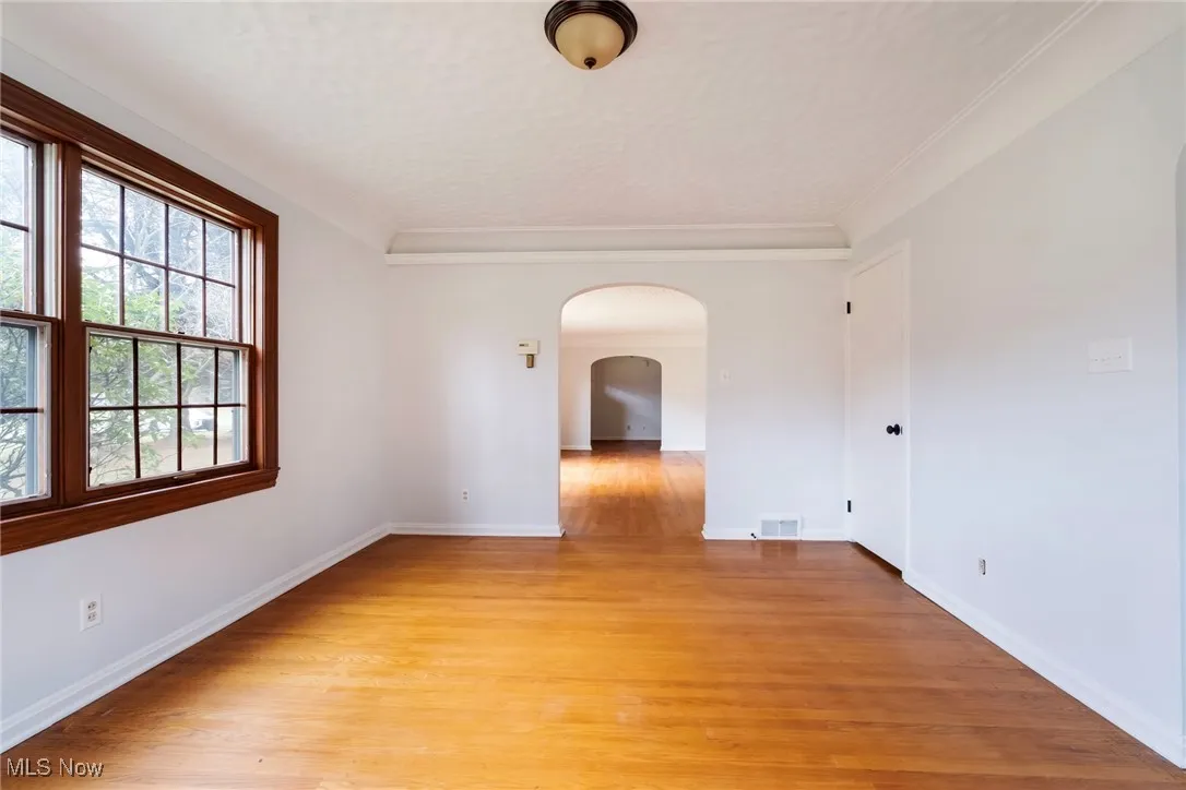 Spare room featuring arched walkways, light wood-style floors, and ornamental molding