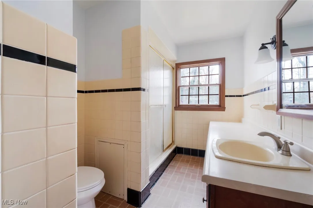 Full bath featuring tile walls, vanity, a stall shower, and a wainscoted wall