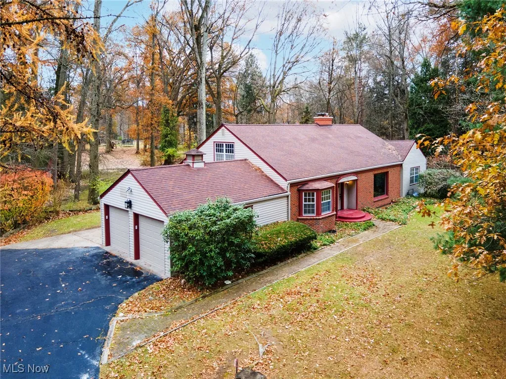 View of front of house with a chimney, brick siding, driveway, a garage, and a front lawn
