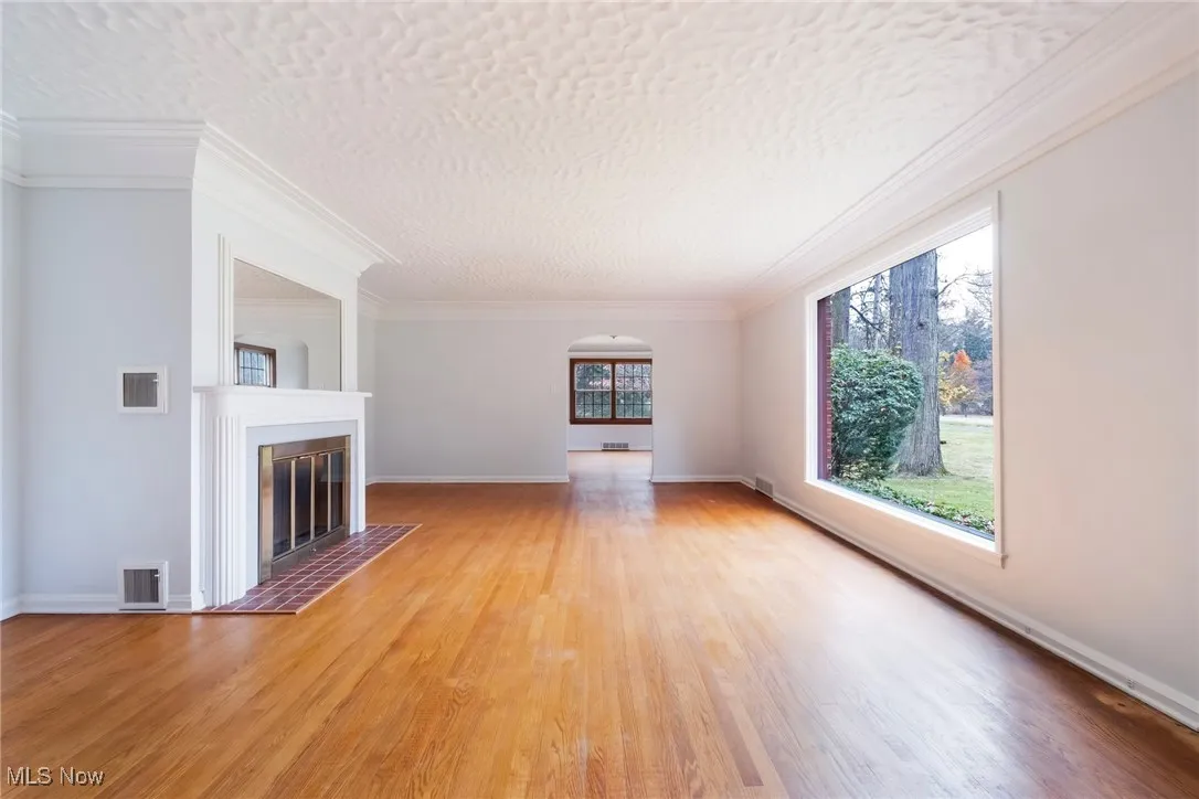 Unfurnished living room featuring crown molding, a glass covered fireplace, wood finished floors, a textured ceiling, and arched walkways