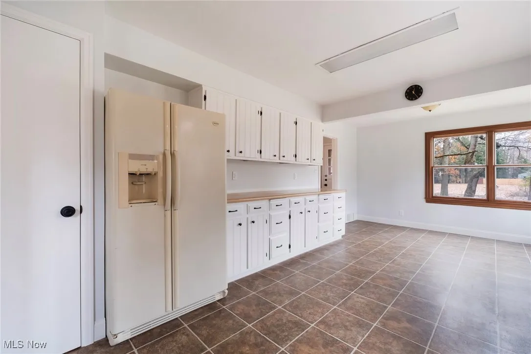 Kitchen with white fridge with ice dispenser, light countertops, and white cabinets