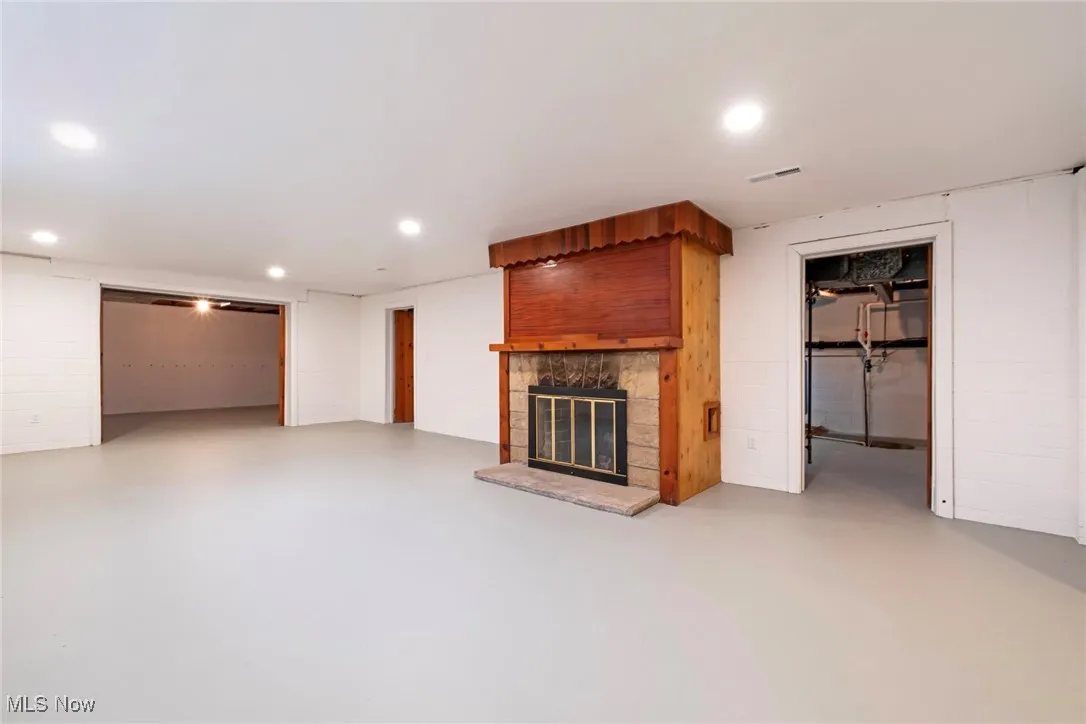 Unfurnished living room featuring concrete block wall, a fireplace, concrete flooring, and recessed lighting