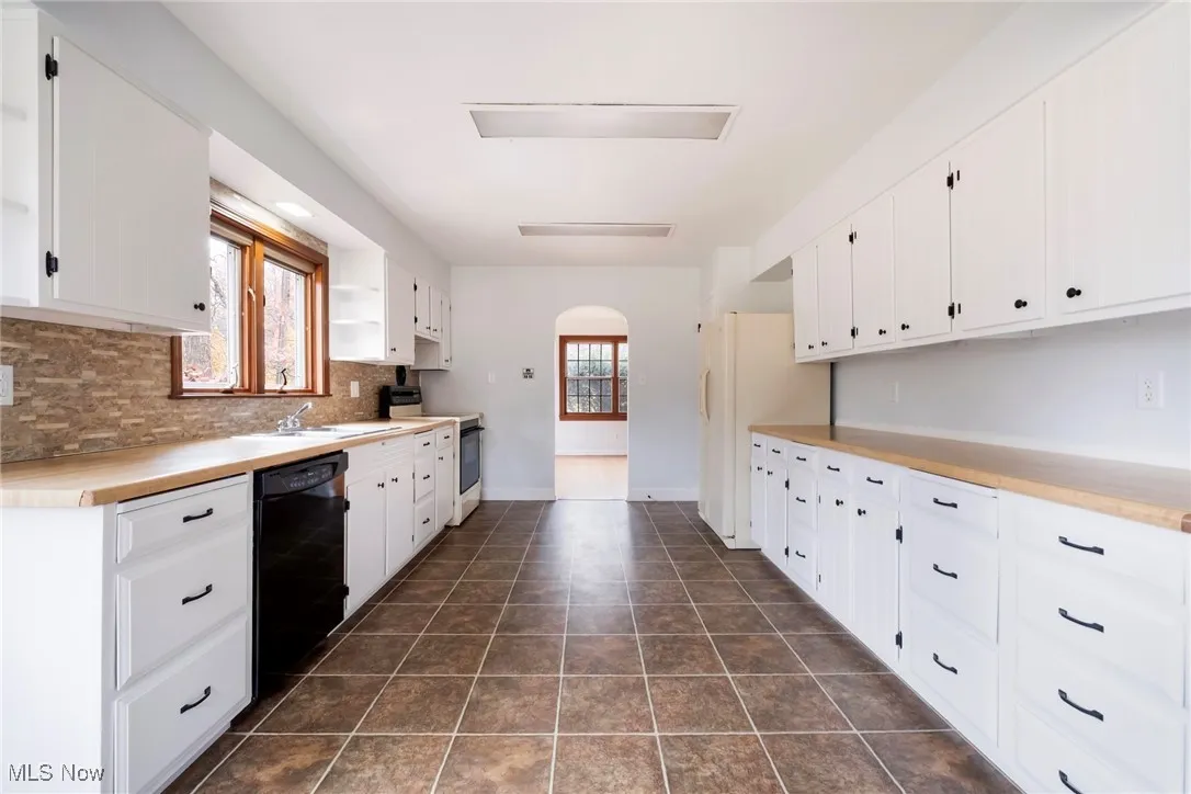 Kitchen featuring arched walkways, wood counters, electric range, black dishwasher, and white cabinets