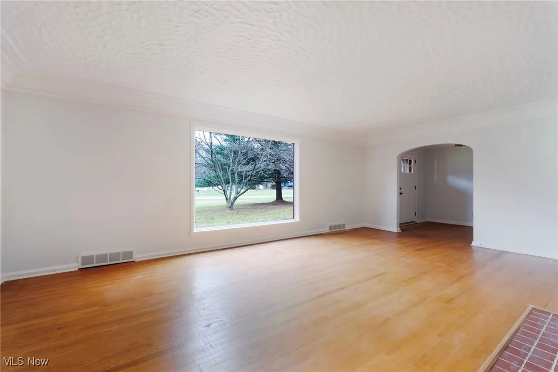 Spare room with arched walkways, light wood-type flooring, crown molding, and a textured ceiling