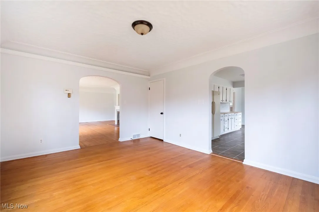 Spare room with arched walkways, light wood-type flooring, ornamental molding, and a textured ceiling