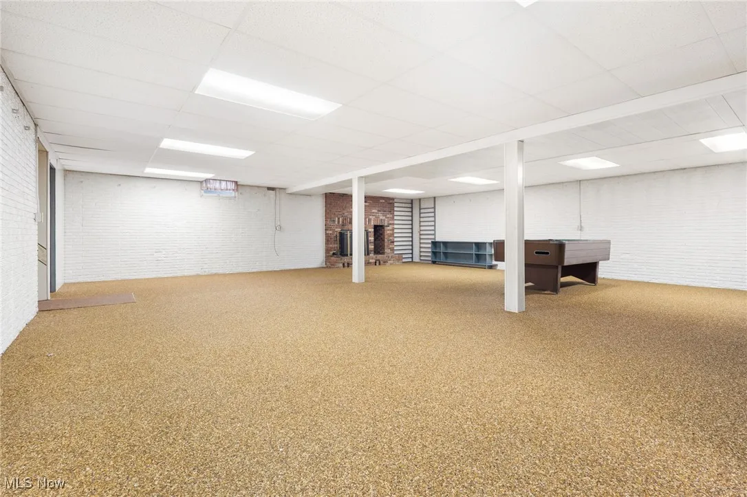 Finished below grade area with naturestone flooring, a drop ceiling, and a brick fireplace