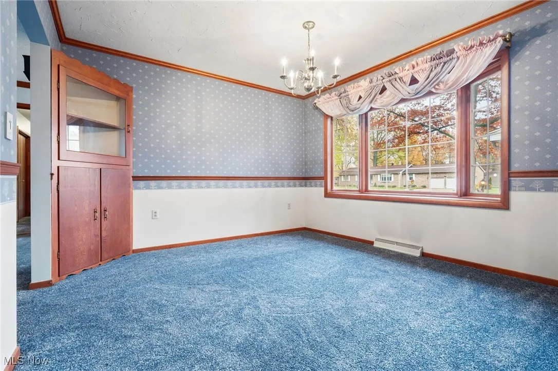 Carpeted dining room with ornamental molding, a chandelier, built-in shelves, and wallpapered walls