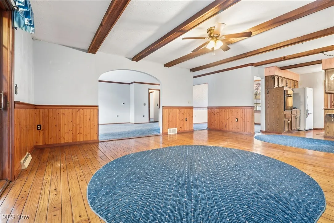 Unfurnished family  room with light wood-style floors, wainscoting, arched walkways, ceiling fan, and beamed ceiling