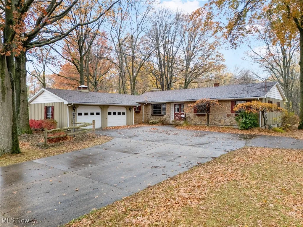 Ranch-style home with a chimney, driveway, an attached garage, and stone siding