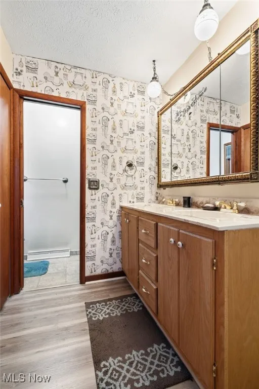 Primary Bathroom featuring a large lighted-closet, a dual sink with vanity, a textured ceiling, light wood-style floors, and baseboard heating
