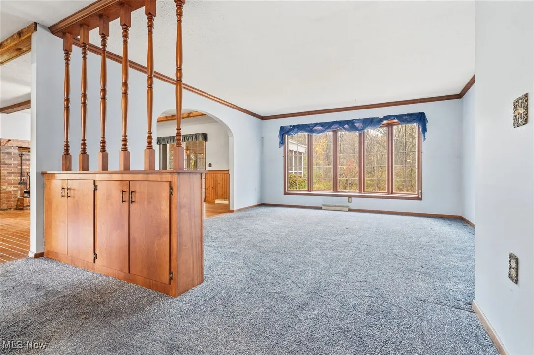 Unfurnished living room featuring light carpet, arched walkways, and crown molding