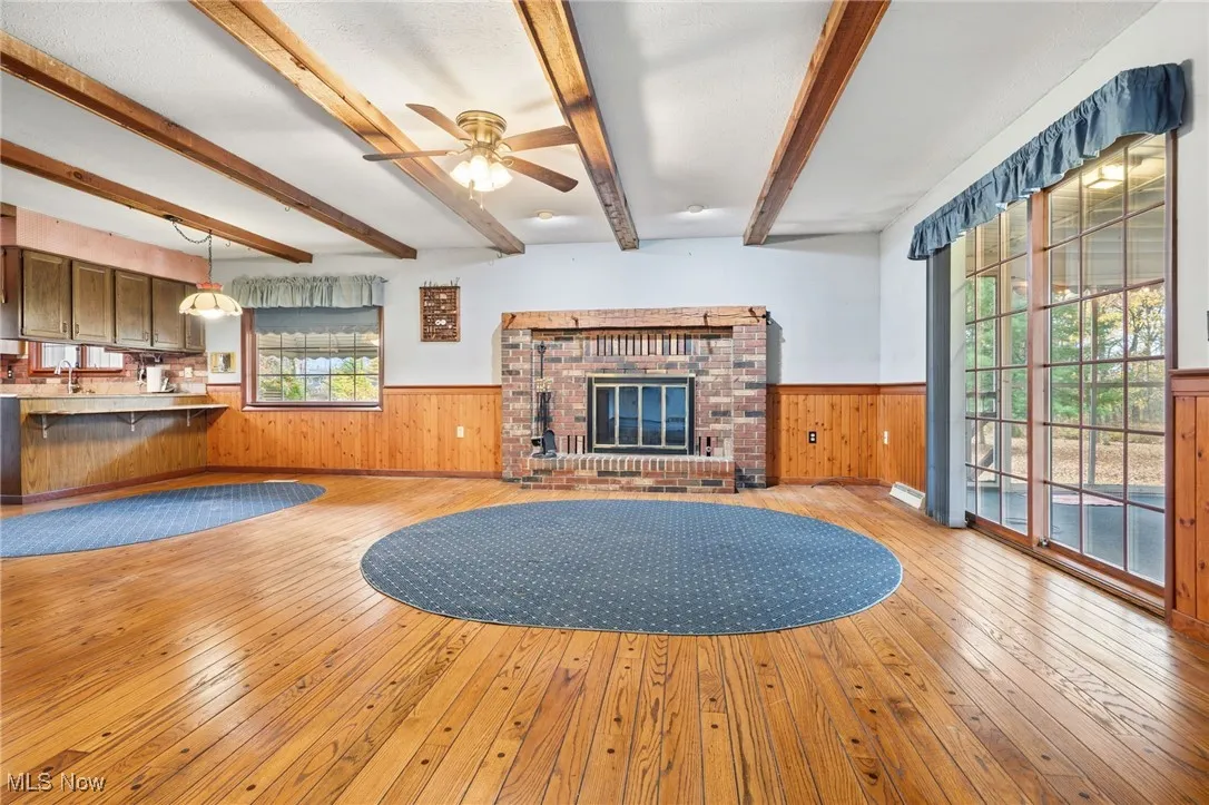 Family room featuring light wood-style floors, wainscoting, ceiling fan, beam ceiling, and a fireplace